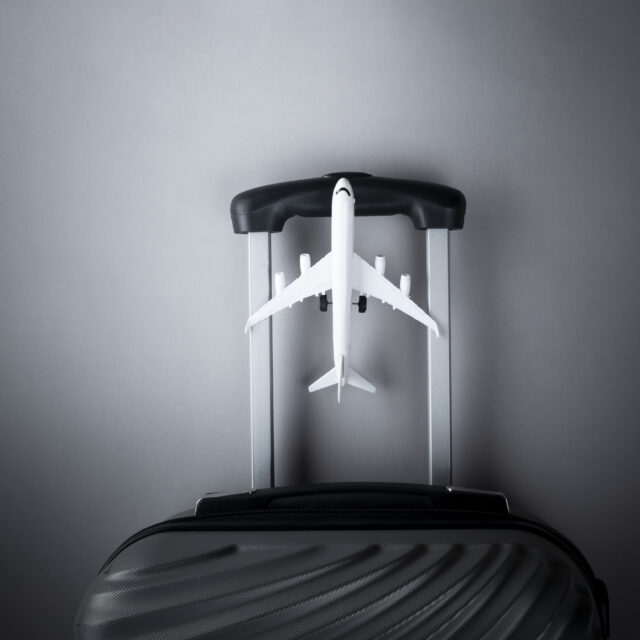 Flat lay grey suitcase with mini airplane on grey background. tr